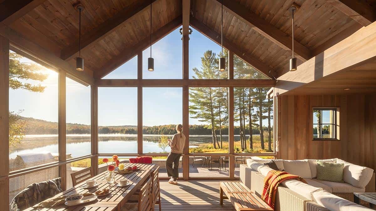 Screened porch with vaulted wood ceiling, dining table, and sectional sofa overlooking a lake