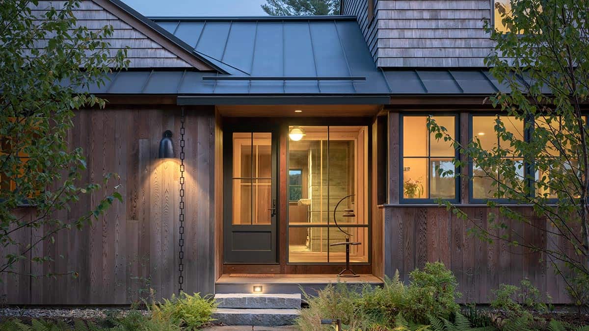 Evening view of a wood-shingled home's entrance with warm interior lighting