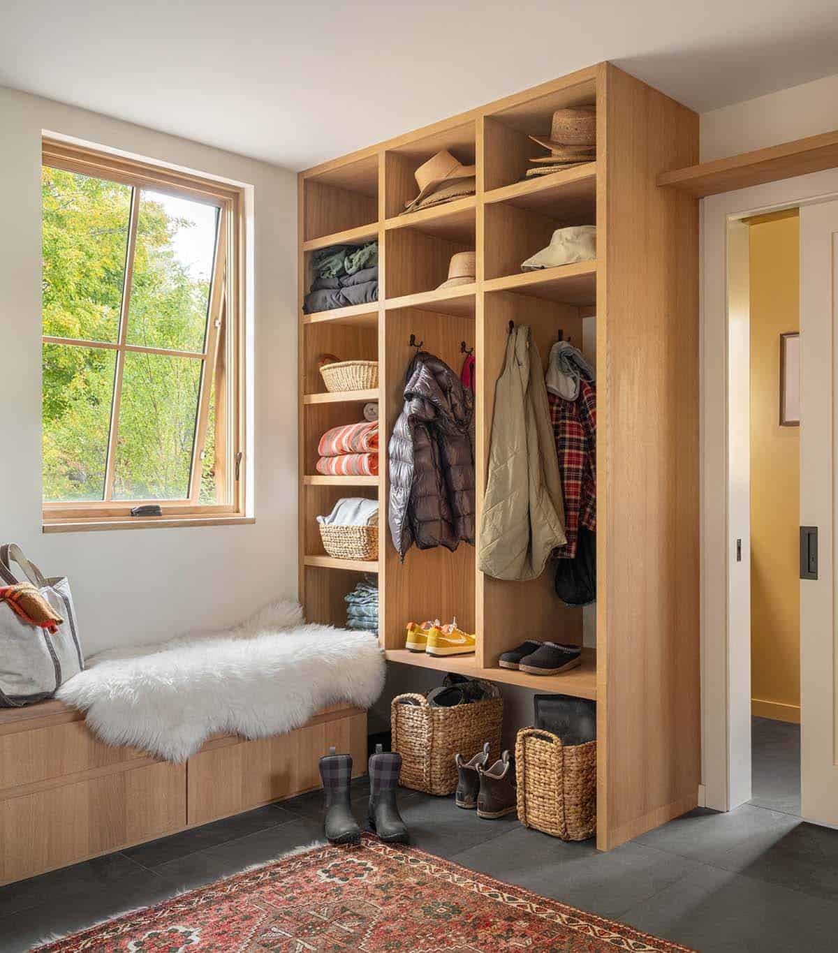 Built-in mudroom storage with cubbies, hanging coats, boots, and a sheepskin-covered bench