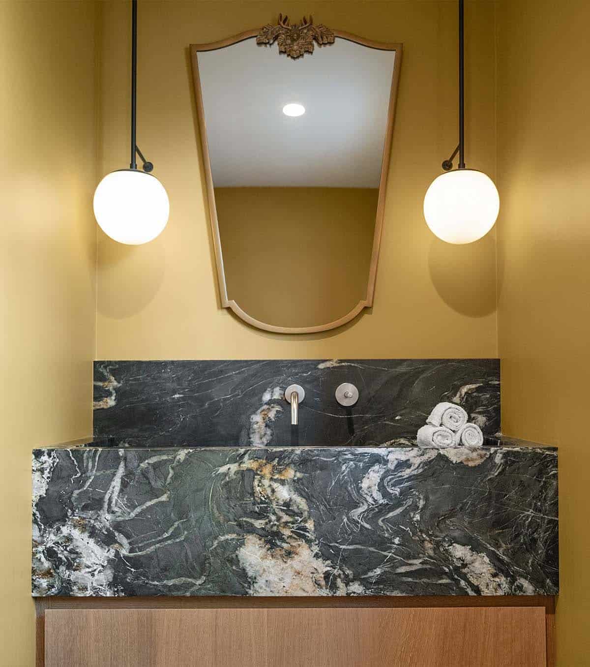 Powder room with dark green marble sink, brass antler mirror, and globe pendant lights