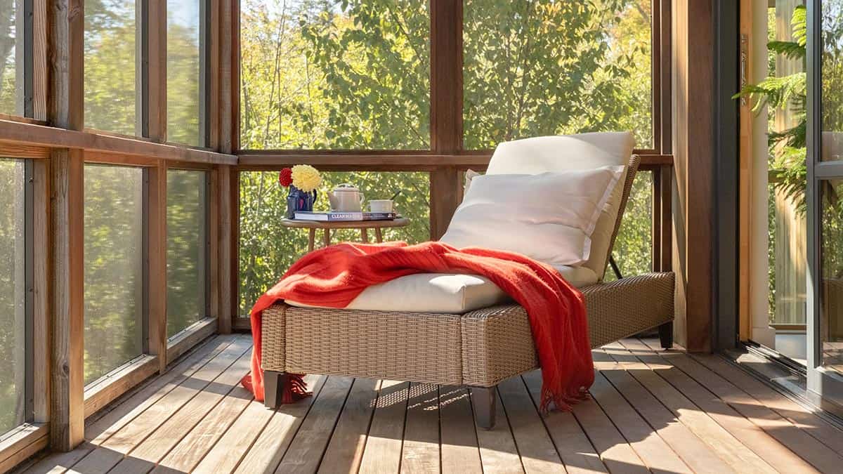 Screened porch corner with a wicker chaise lounge and red throw blanket