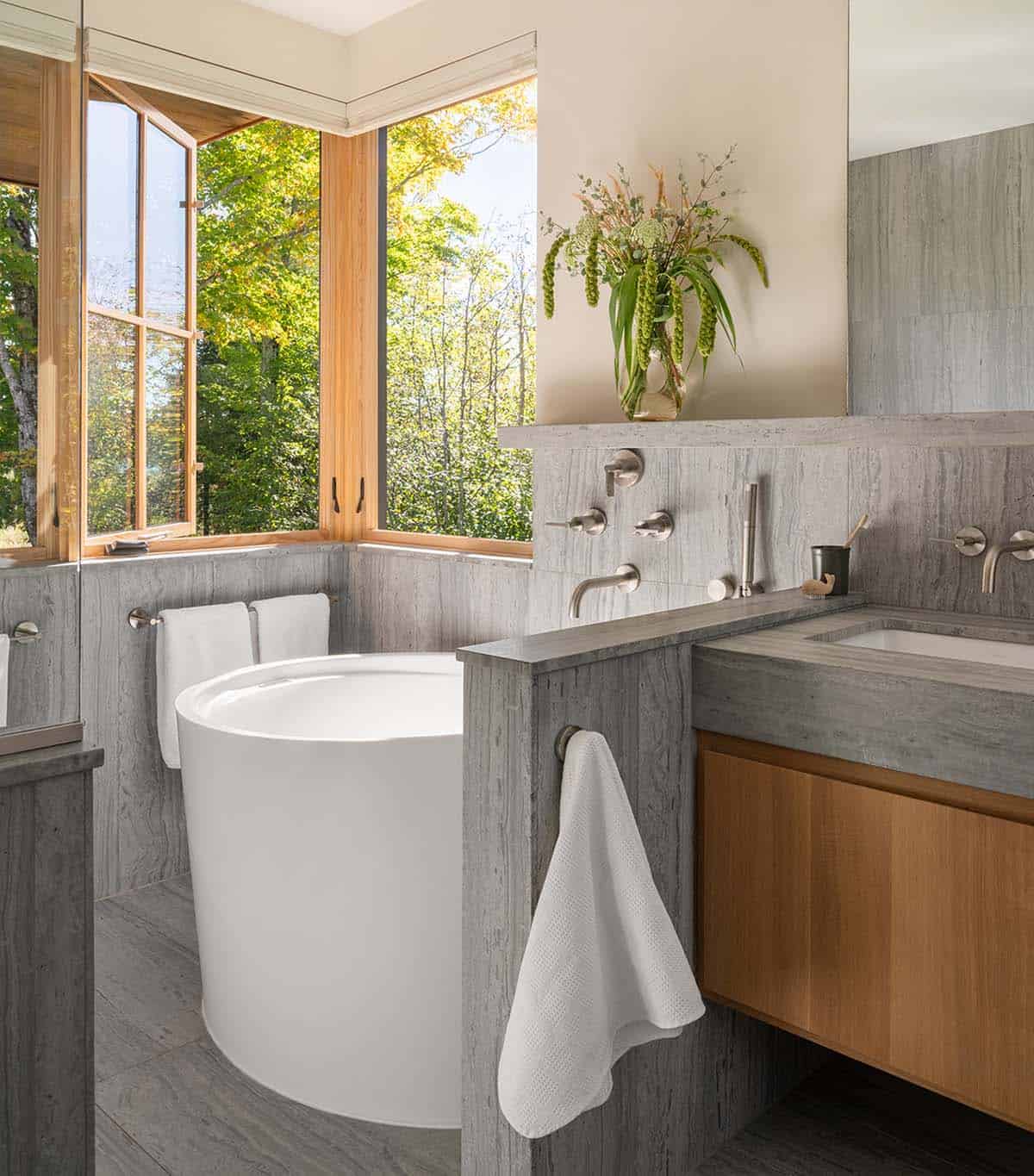 Bathroom with freestanding soaking tub, stone walls, and corner windows framing trees