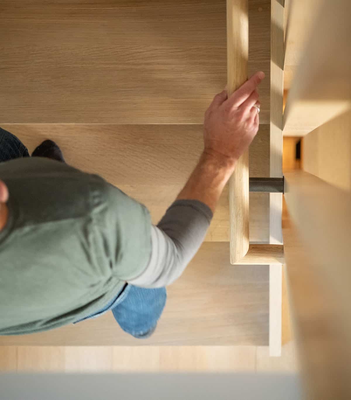 Overhead view of a hand resting on a wooden stair railing
