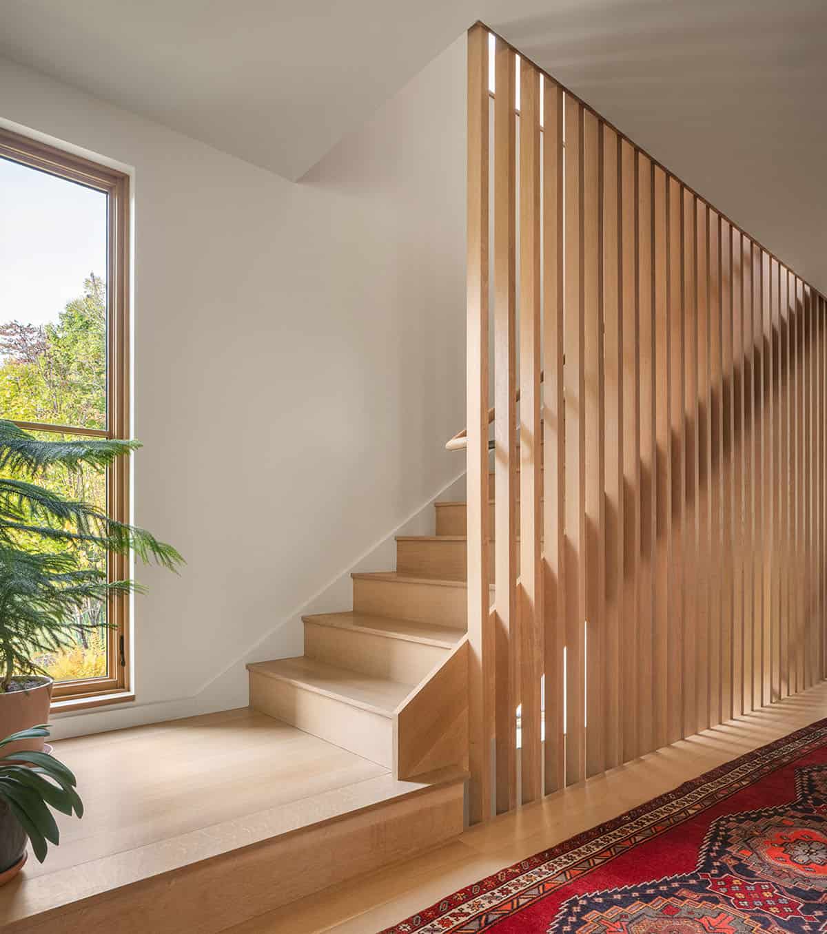 Wood-slatted staircase with a red patterned runner rug and large window