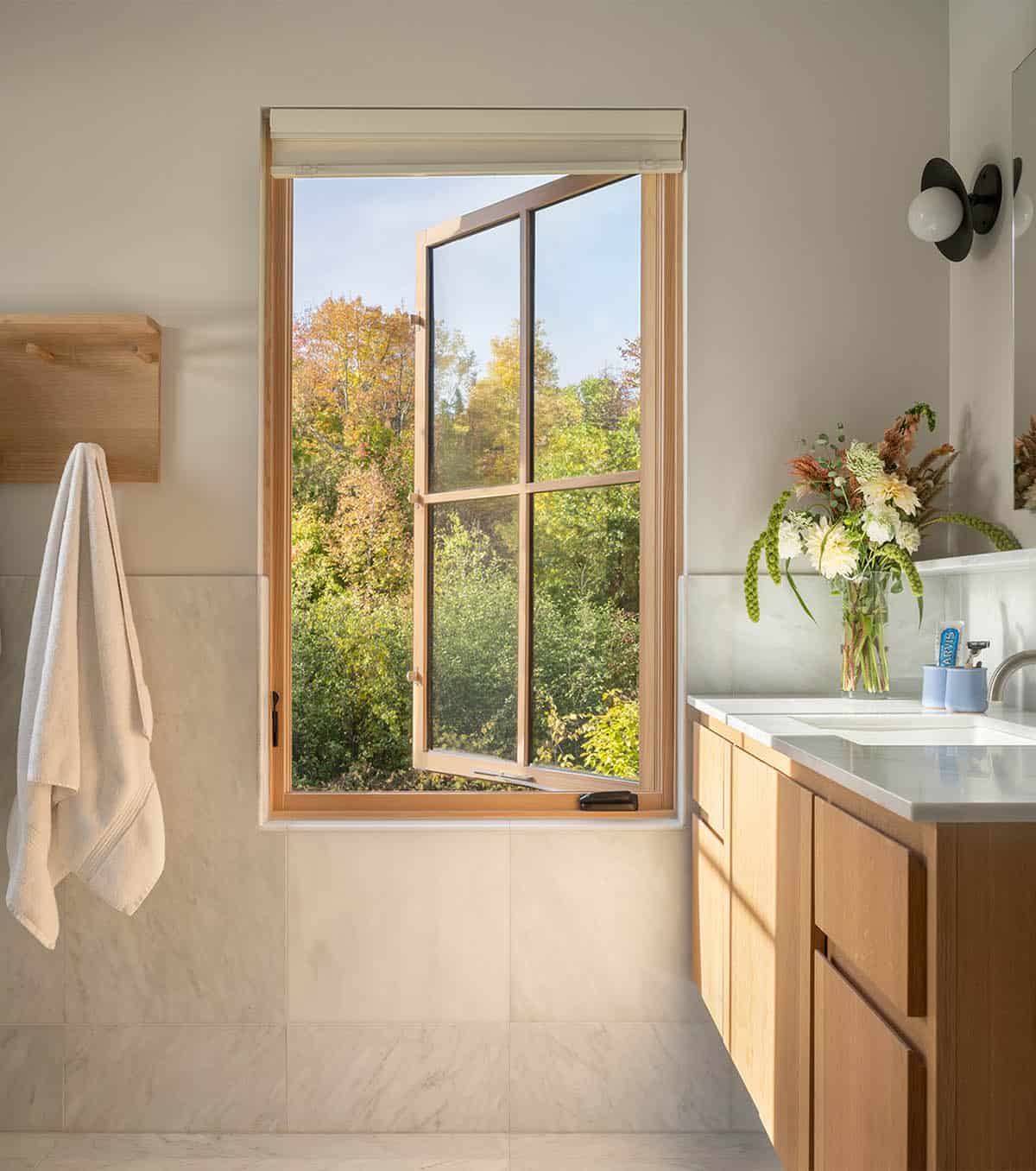 Bathroom with marble tile, wood vanity, and an open casement window showing autumn trees