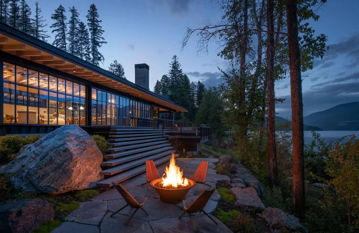 House glowing at dusk with fire pit and stone patio