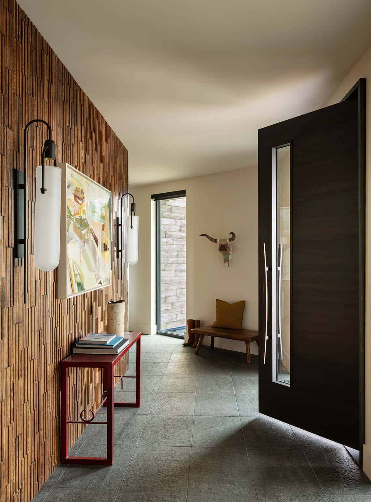 Entryway with slatted wood accent wall, red console table, and dark pivoting front door