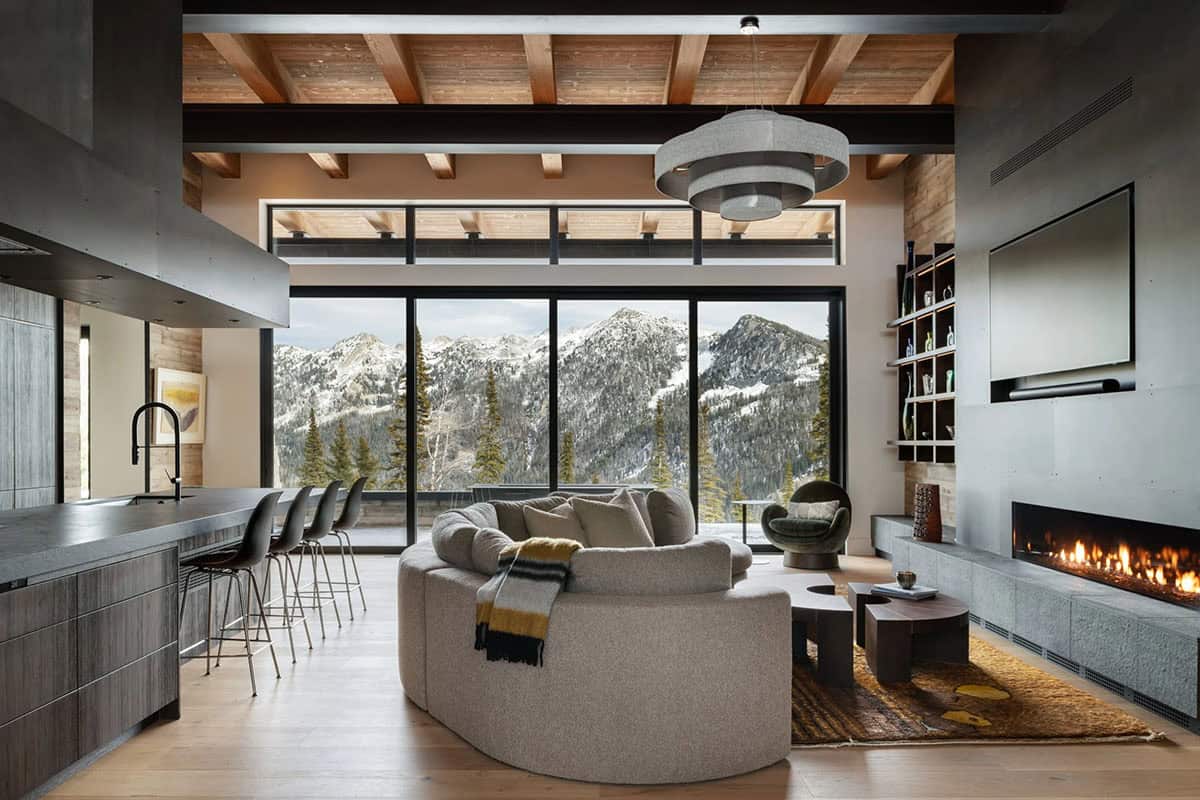 Open-concept living room and kitchen with round sofa, fireplace, and floor-to-ceiling mountain views