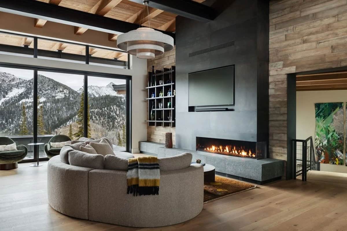 Living room with curved sectional sofa, wood-clad wall, and linear gas fireplace facing mountain windows