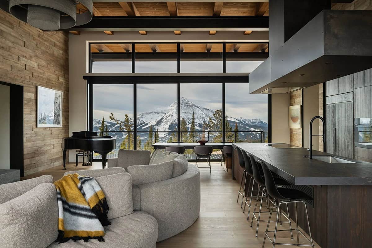 Great room with grand piano, curved sofa, and kitchen island overlooking a snowy peak