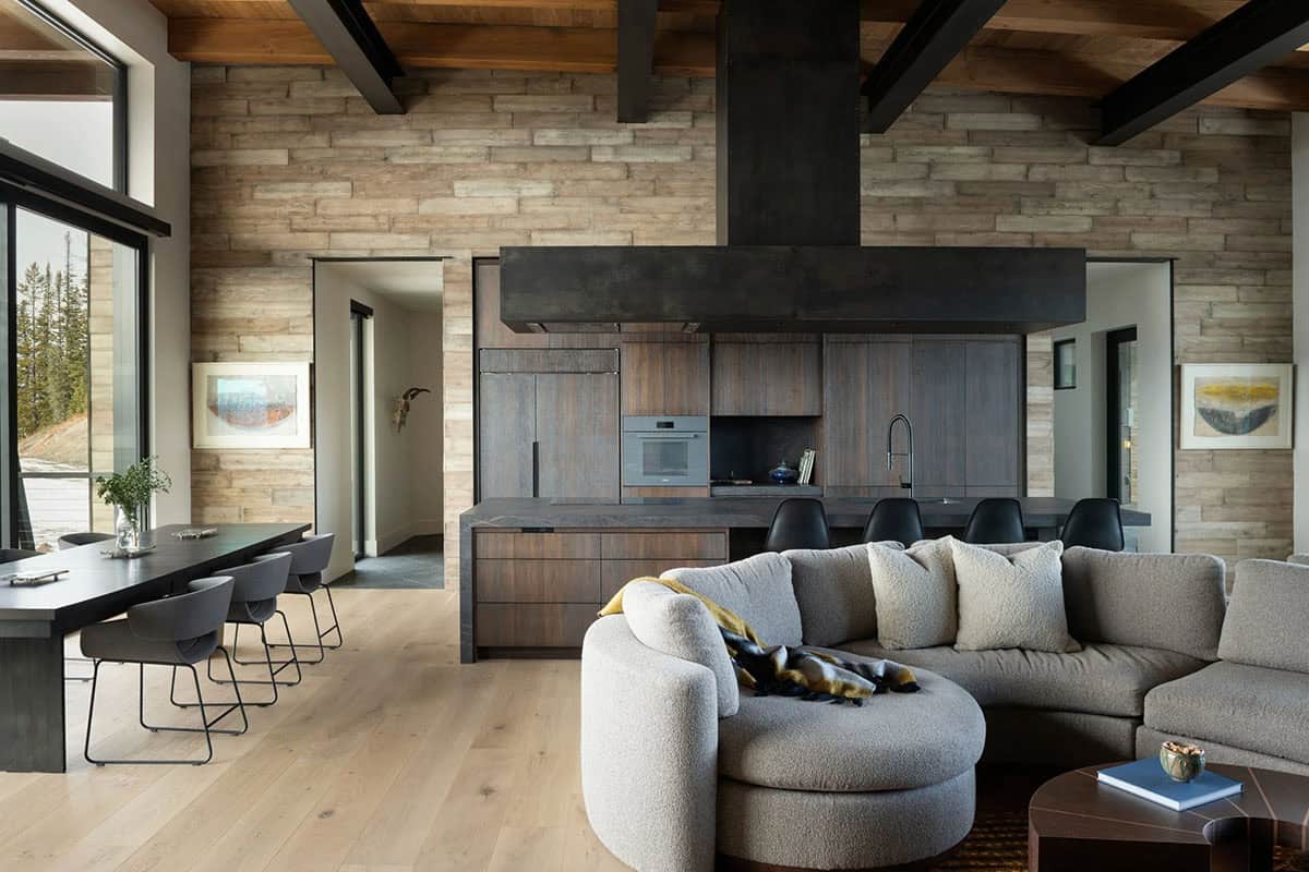 Open living and dining area with stone-tiled wall, dark wood kitchen, and beamed ceiling