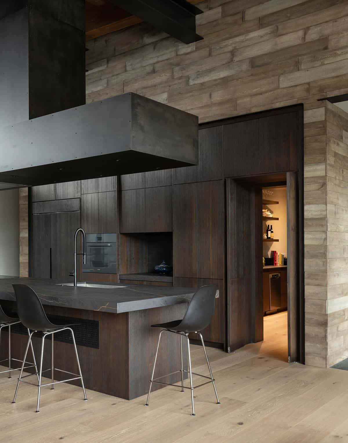 Dark wood kitchen island with bar stools beside an open door to a wine pantry