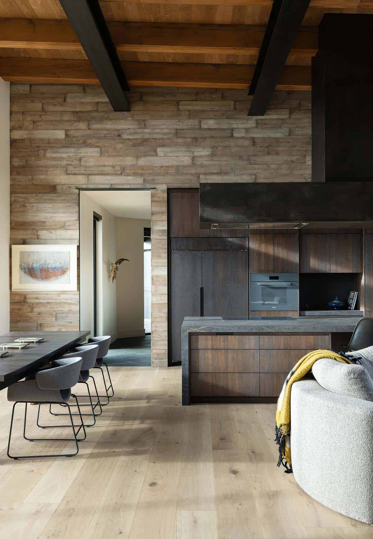 Dining table and kitchen island with stone accent wall and exposed wood ceiling beams
