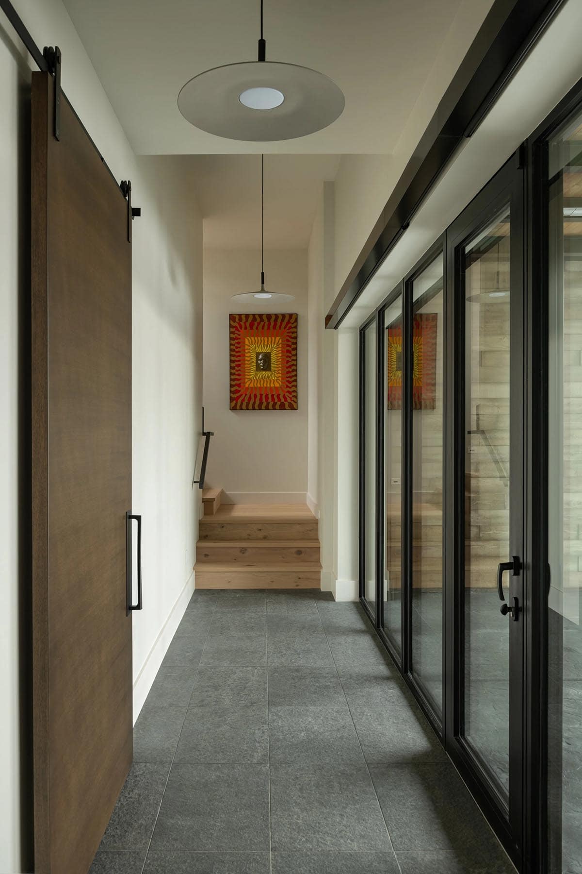 Hallway with sliding barn door, glass walls, wooden steps, and colorful framed artwork