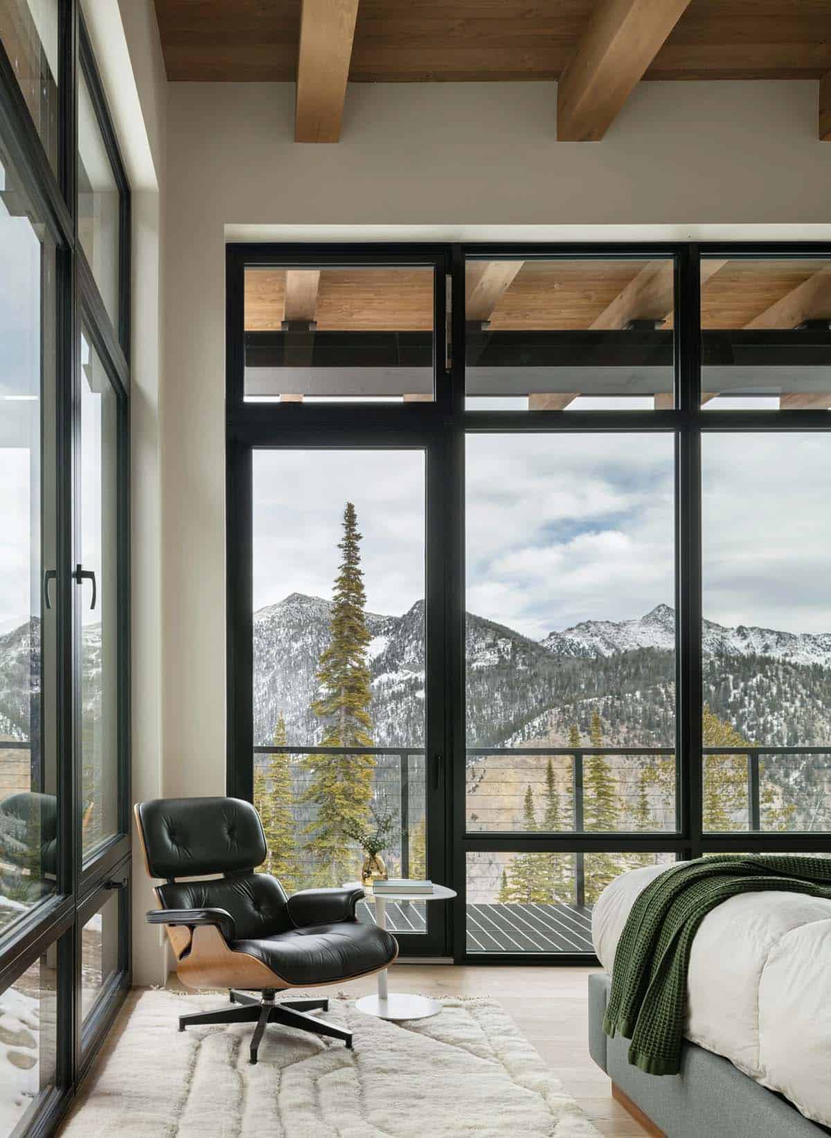 Bedroom corner with black leather lounge chair beside floor-to-ceiling windows overlooking mountains
