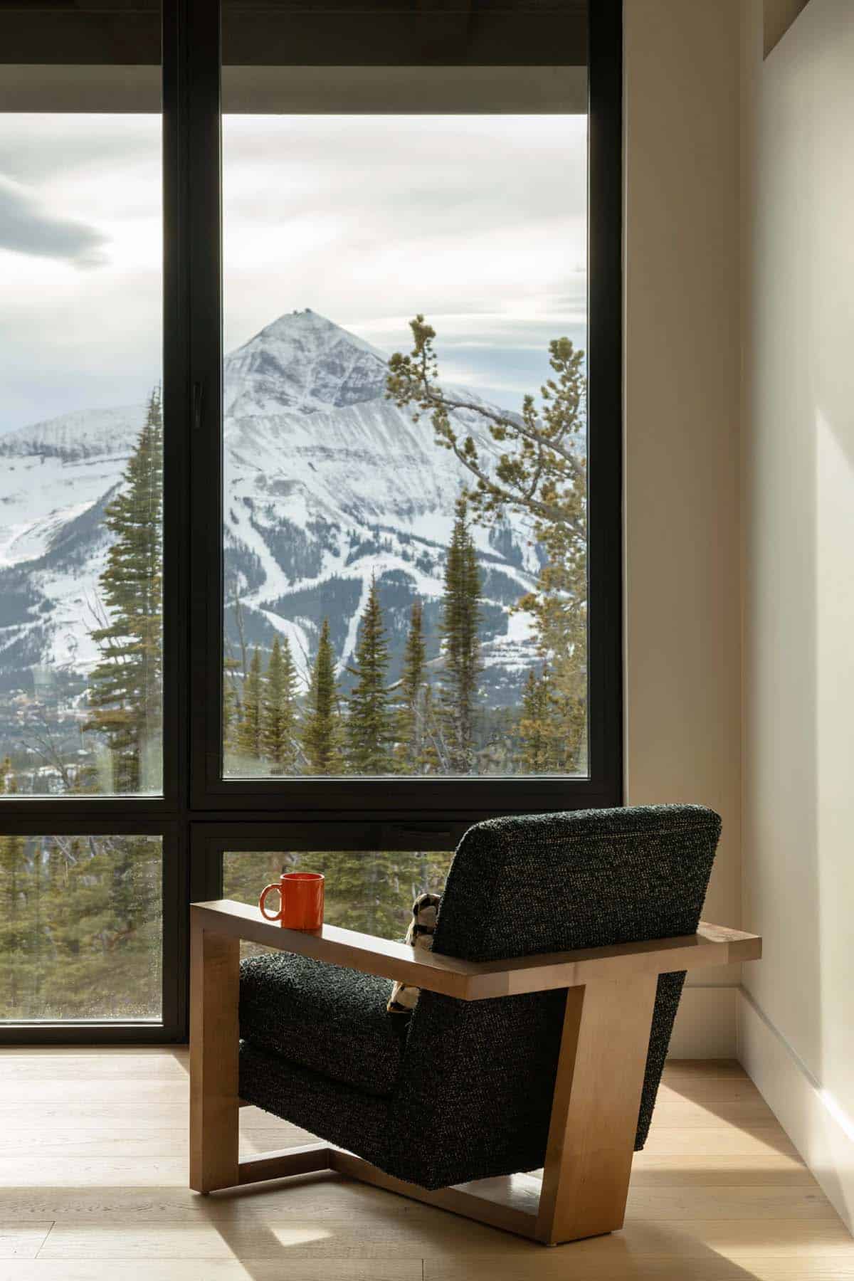 Cozy armchair with a mug on its armrest facing a large window with mountain and ski slope views