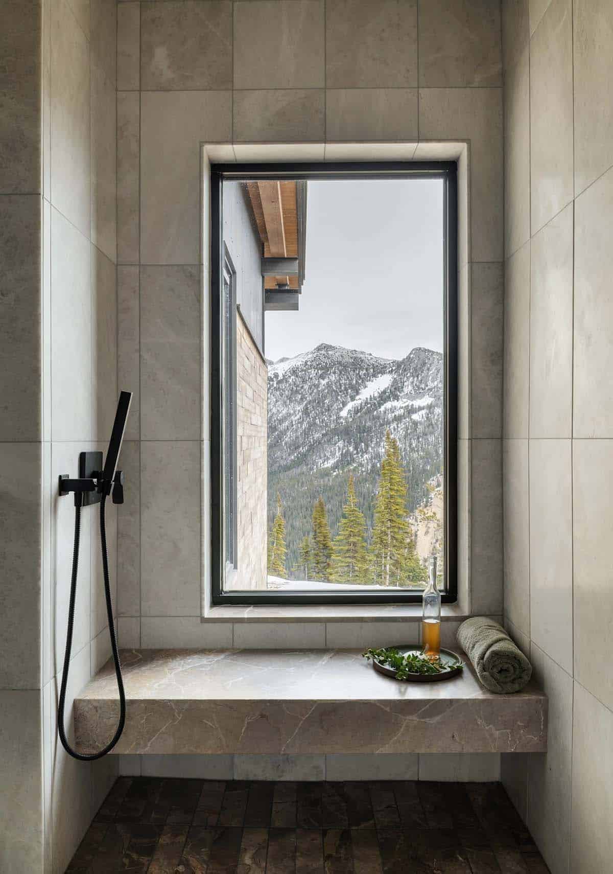 Spa-style shower nook with stone bench, black fixtures, and a window framing snowy peaks