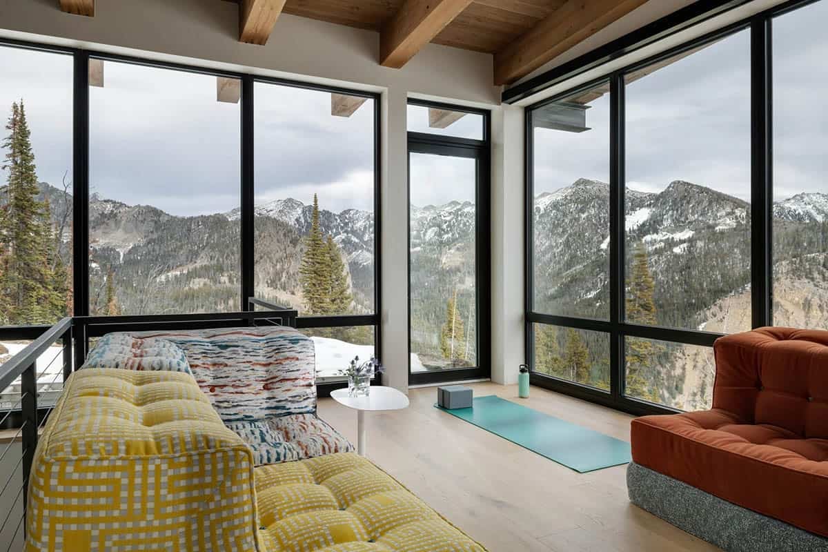 Upstairs lounge with patterned sofas, yoga mat, and panoramic wraparound mountain windows
