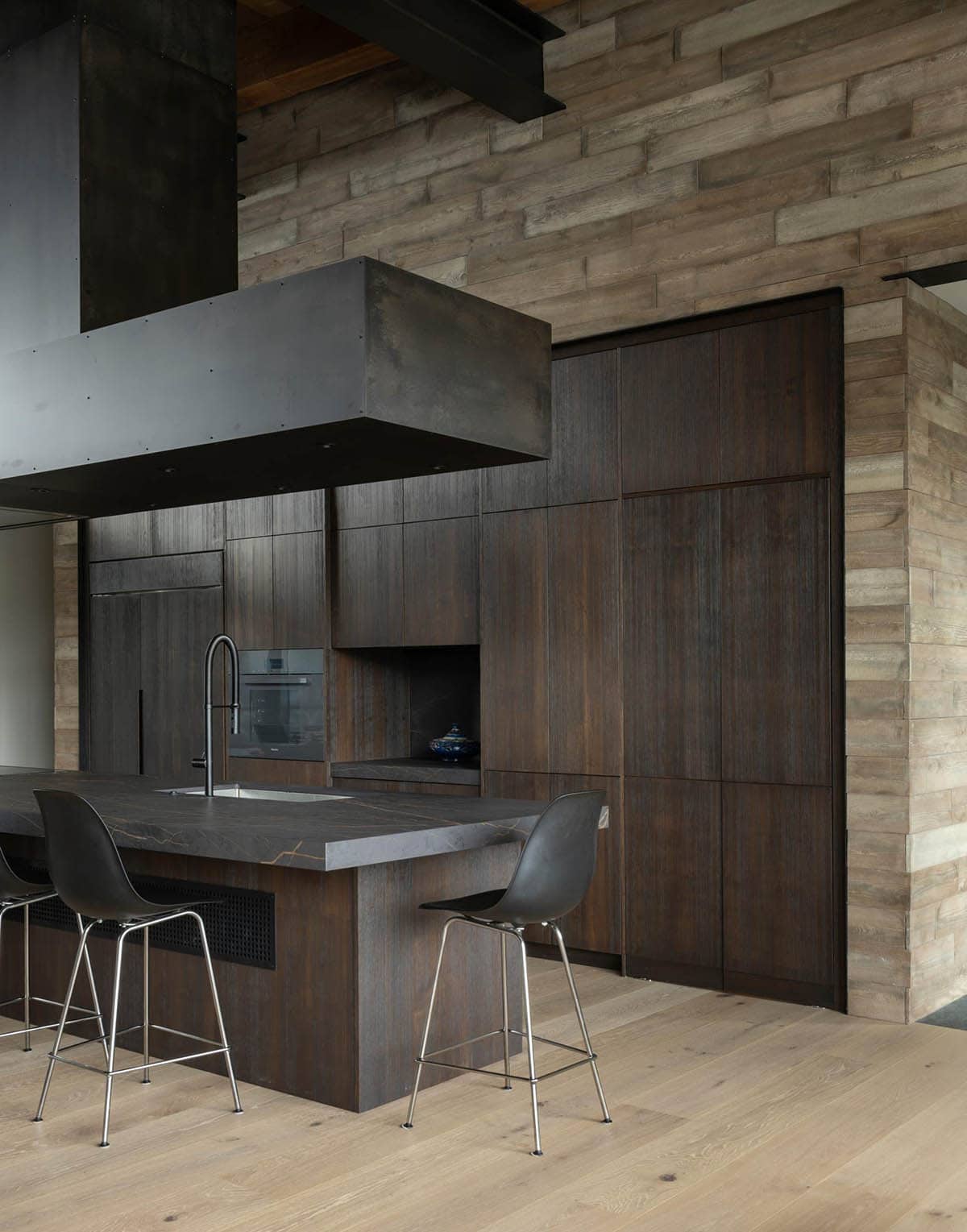 Dark wood kitchen cabinetry with black stone island, bar stools, and stone accent wall