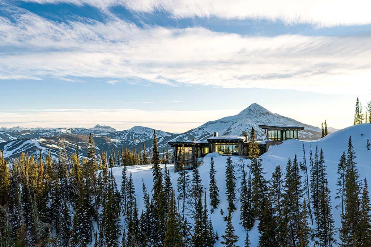 Aerial view of the mountain home glowing at dusk with a prominent snow-covered peak behind it