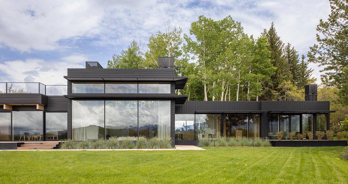 Black-clad modern mountain house exterior with floor-to-ceiling windows and green lawn