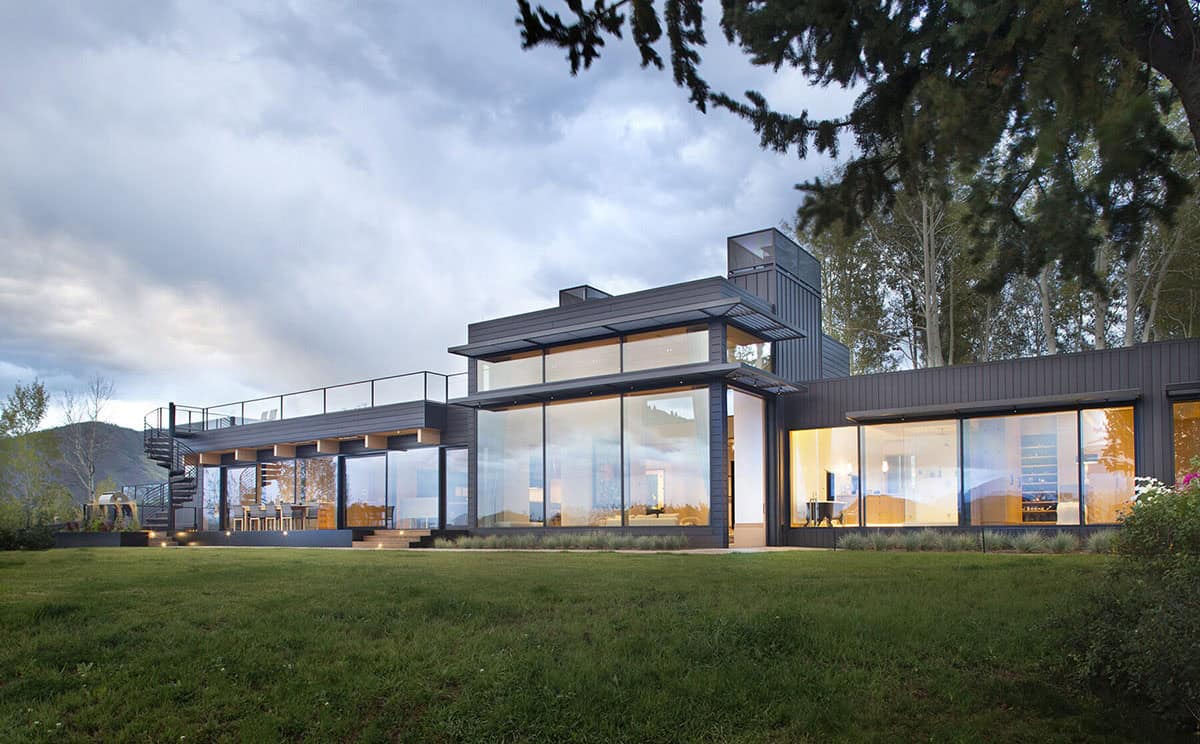 Dusk view of black modern home with glowing interior lights and spiral staircase to rooftop deck