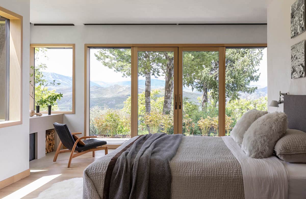 Bedroom with wall-to-wall windows overlooking trees and mountains