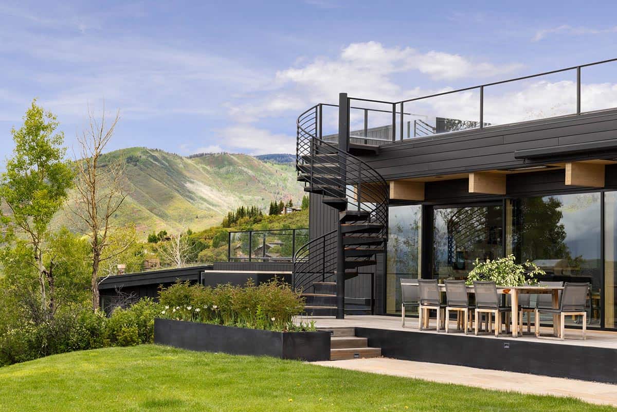 Black spiral staircase leading to rooftop deck beside outdoor dining area with mountain backdrop