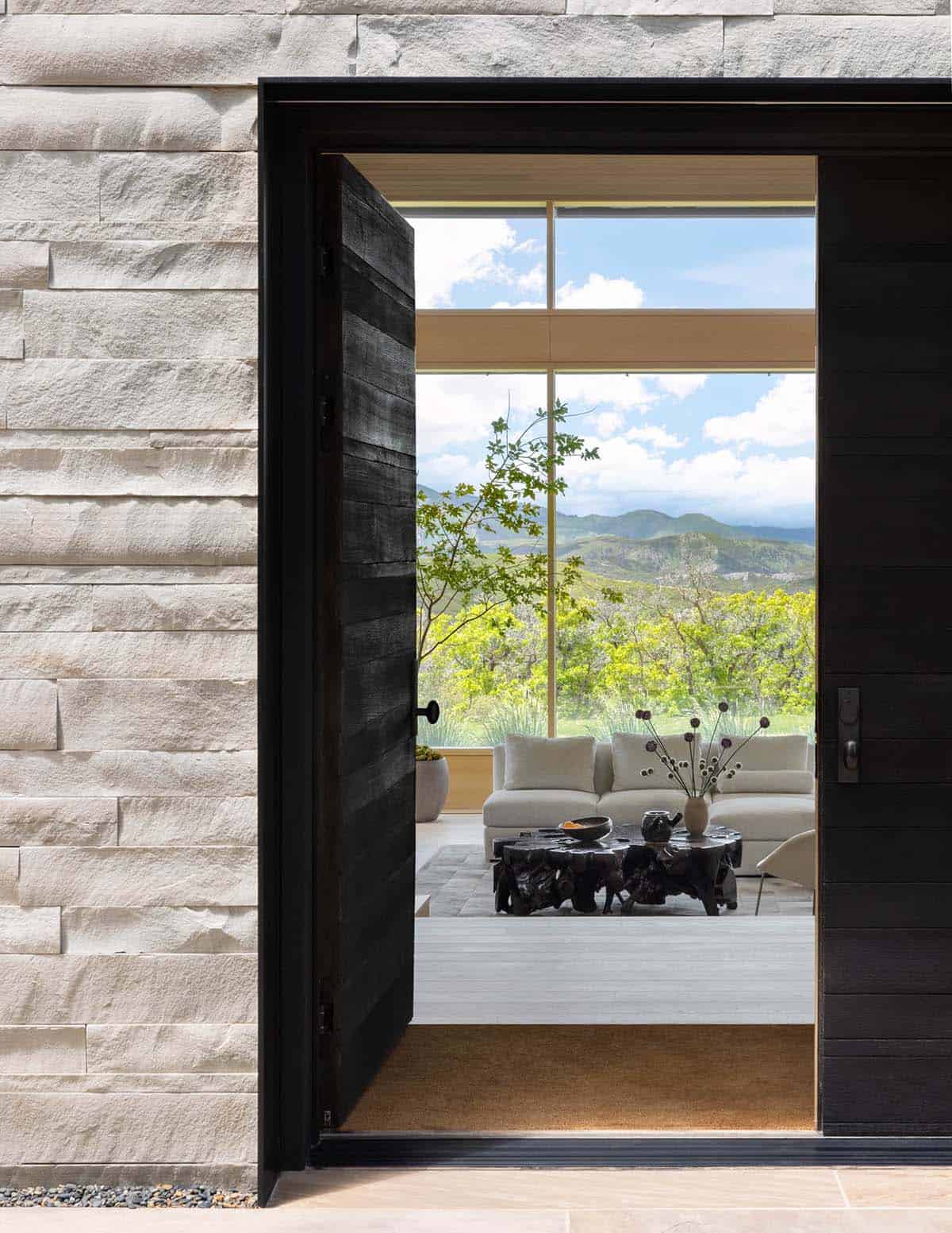 Open dark wood door showing living room and mountain view through stone facade