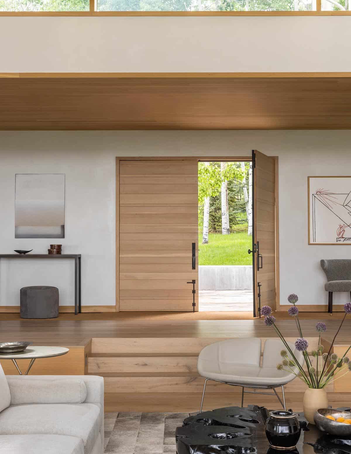 Wood-paneled entryway with open door leading to aspen-lined lawn