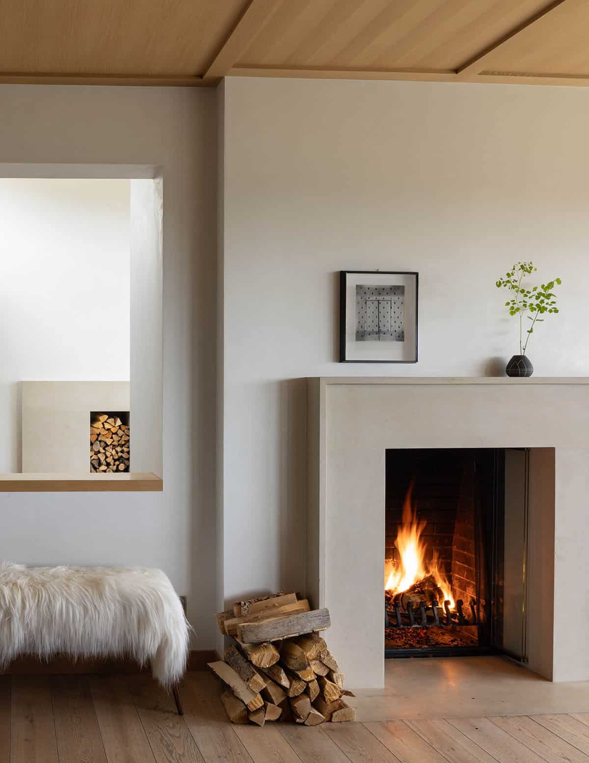 Minimalist stone fireplace nook with stacked firewood and fur bench