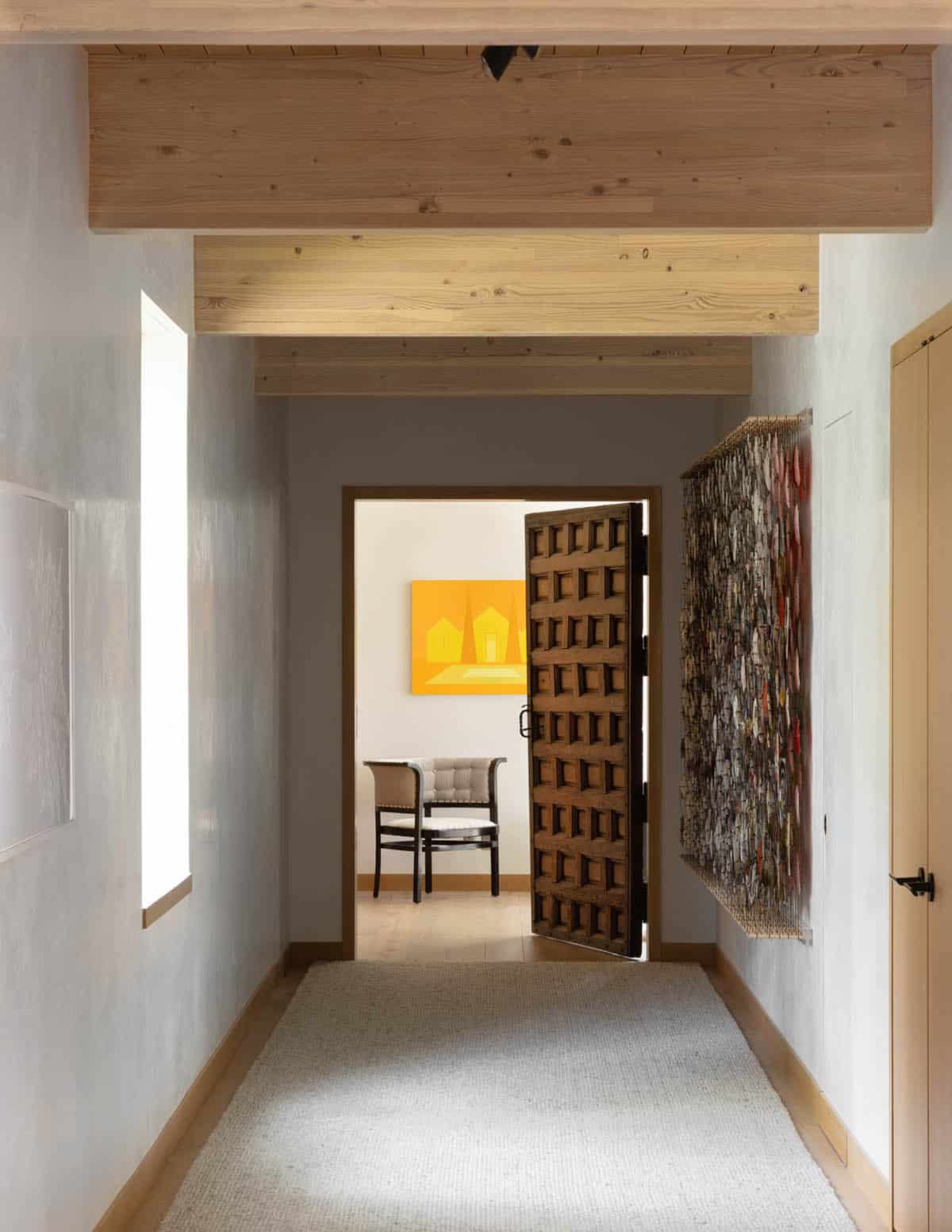 Hallway with carved wood door opening to a room with a yellow abstract painting