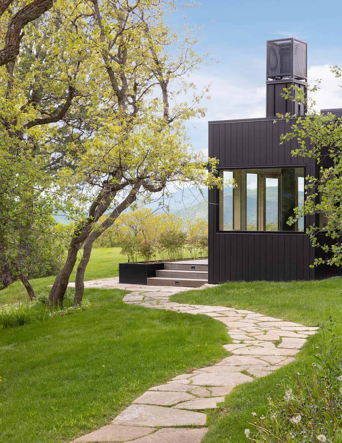 Black house exterior with stone path winding through a grassy yard and trees