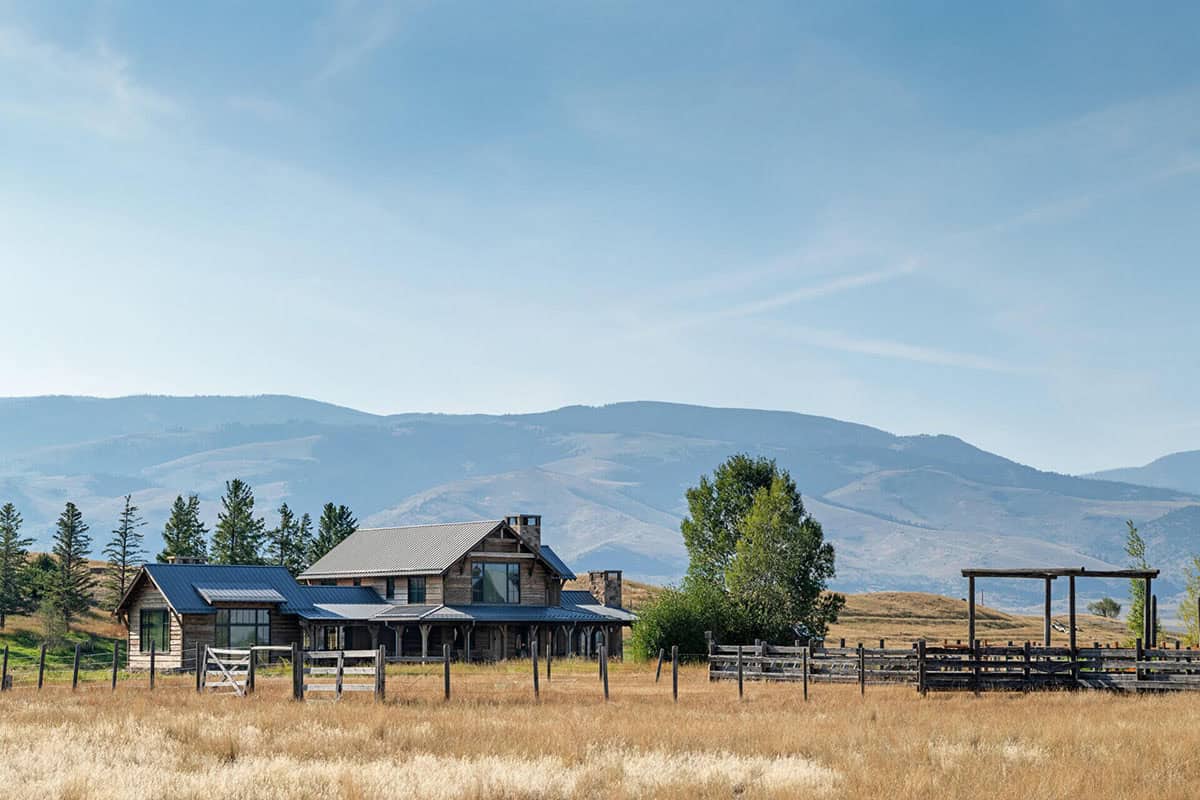 Rustic ranch house with metal roof nestled in a Montana valley below hazy mountains