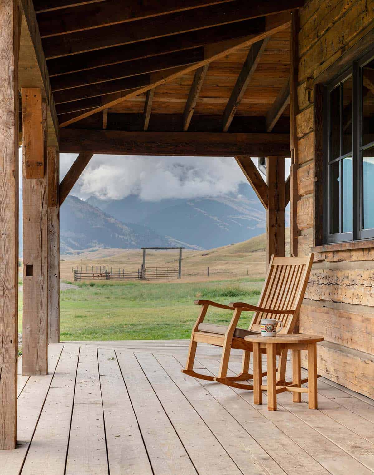 Covered wood porch with a rocking chair overlooking fenced pasture and mountains