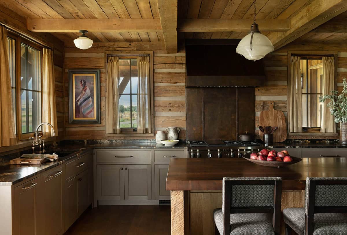 Rustic kitchen with log walls, dark countertops, and vintage schoolhouse pendant lights
