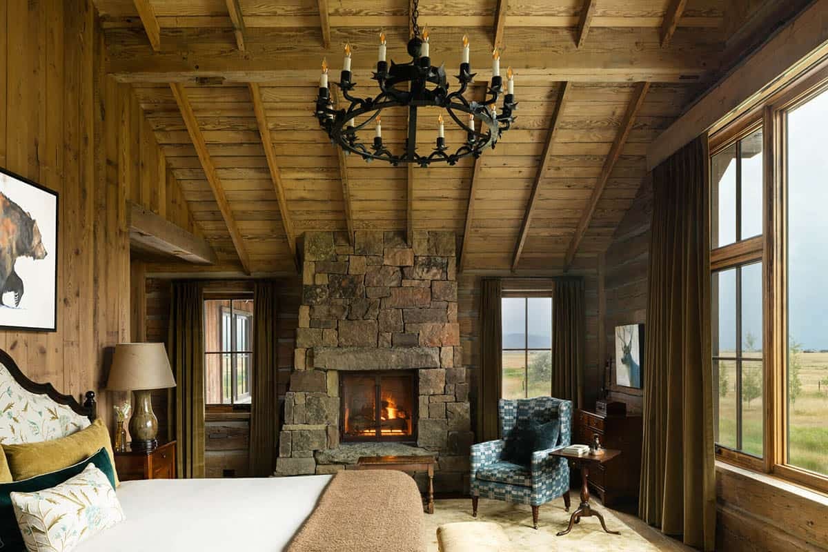 Bedroom with stone fireplace, iron chandelier, and large window overlooking fields