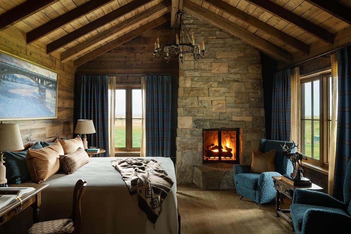 Bedroom with stone corner fireplace, blue armchairs, and plaid curtains