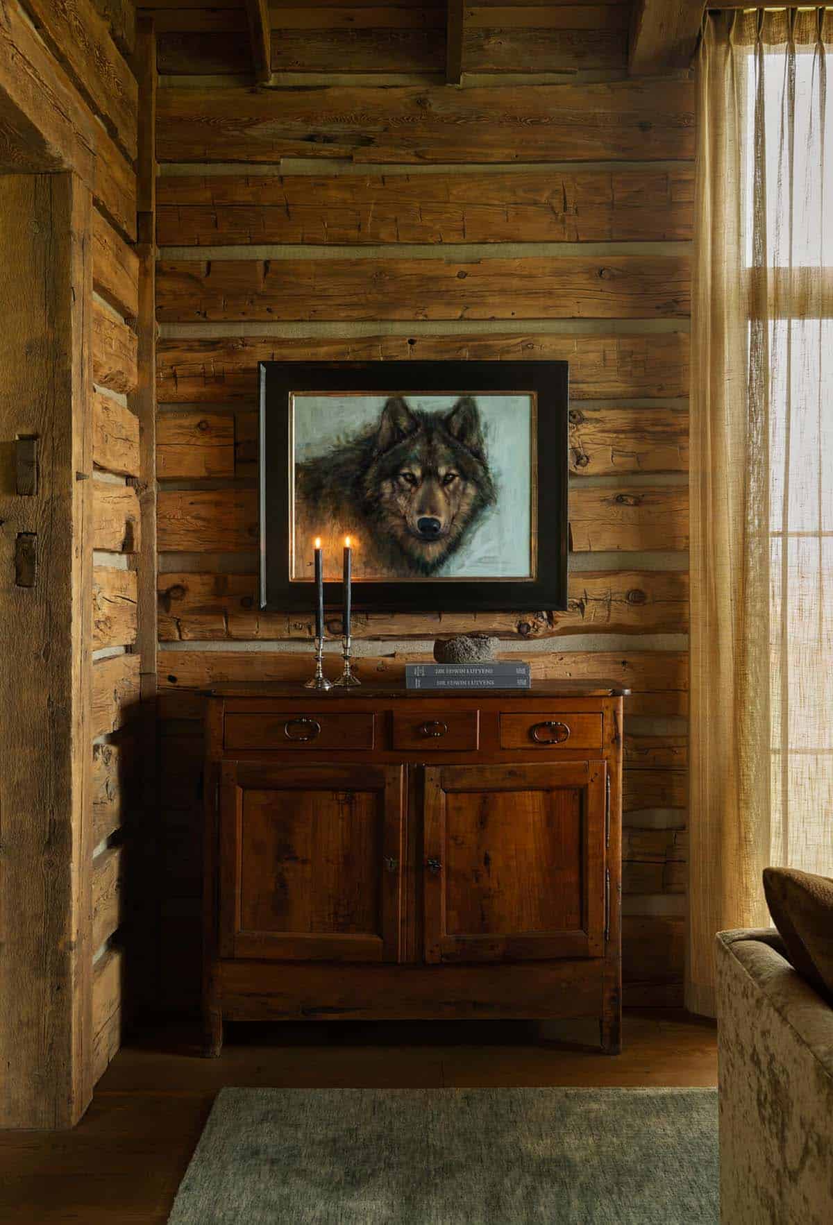 Antique wood cabinet with a wolf painting and lit candlesticks against a log wall