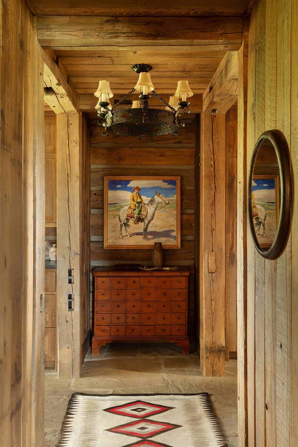 Log hallway with an antique chest, cowboy painting, and Navajo-style rug