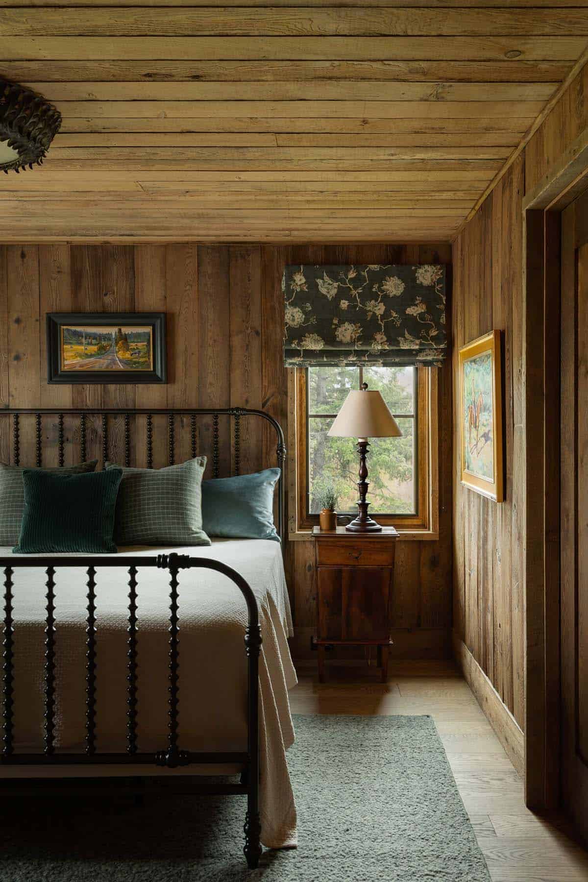 Wood-paneled bedroom with iron bed frame, green pillows, and window nook lamp