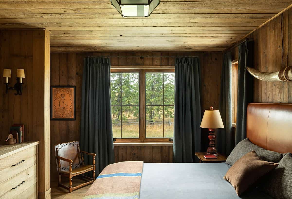 Bedroom with leather headboard, mounted horns, and forest-view windows
