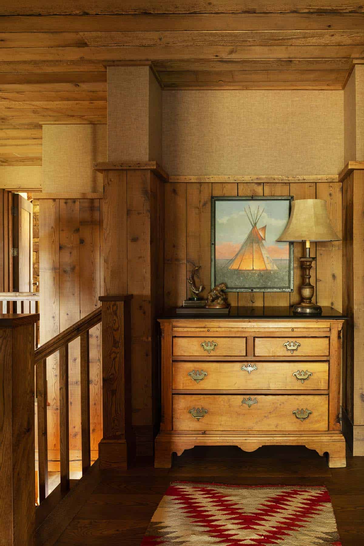 Antique dresser with a teepee painting and lamp beside a wood staircase landing