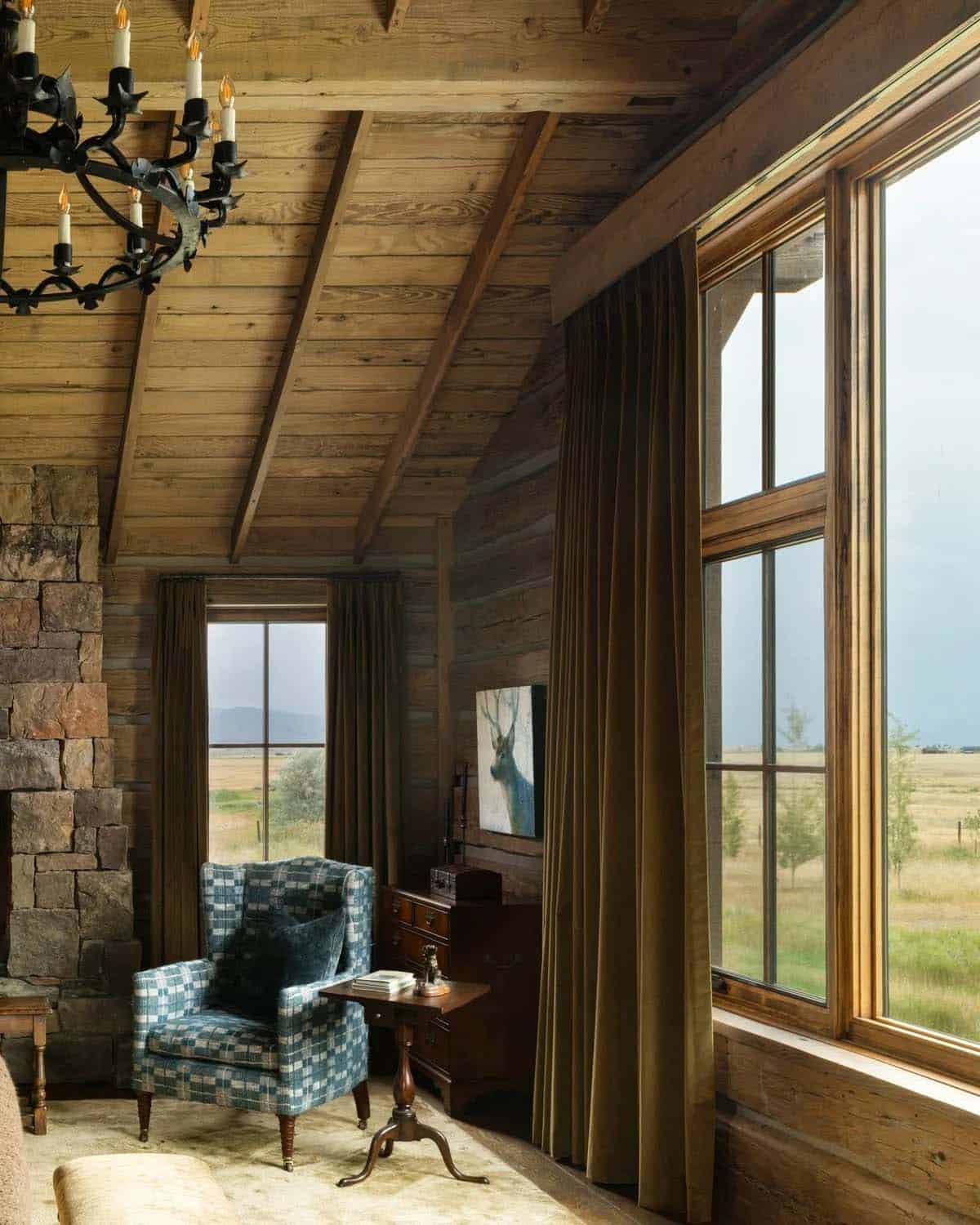 Bedroom corner with plaid armchair, deer painting, and large windows overlooking open fields