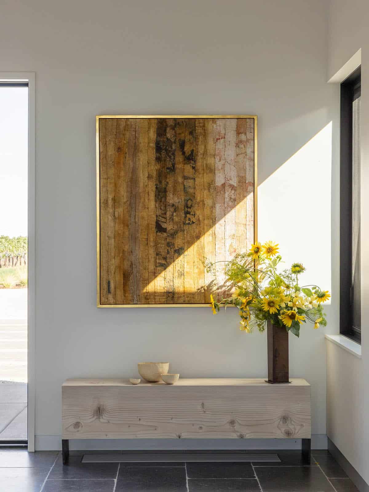 Entryway with abstract artwork, wood bench, and sunflower arrangement