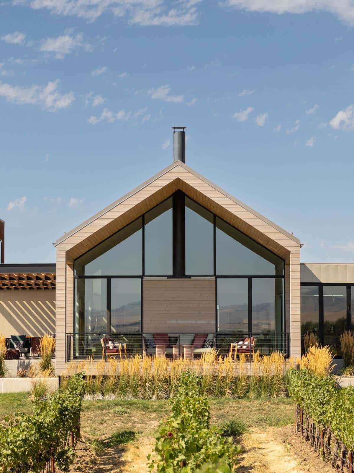 Gabled glass facade with wood siding framed by vineyard rows