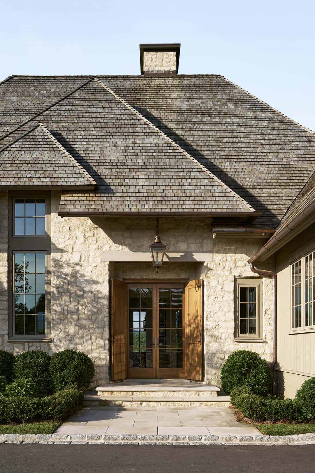 Arched wood entry doors framed by cut stone facade and lantern