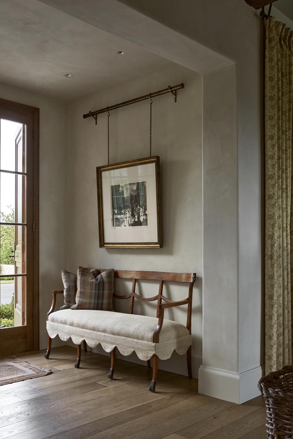 Entry bench beneath hanging framed artwork and scalloped linen upholstery