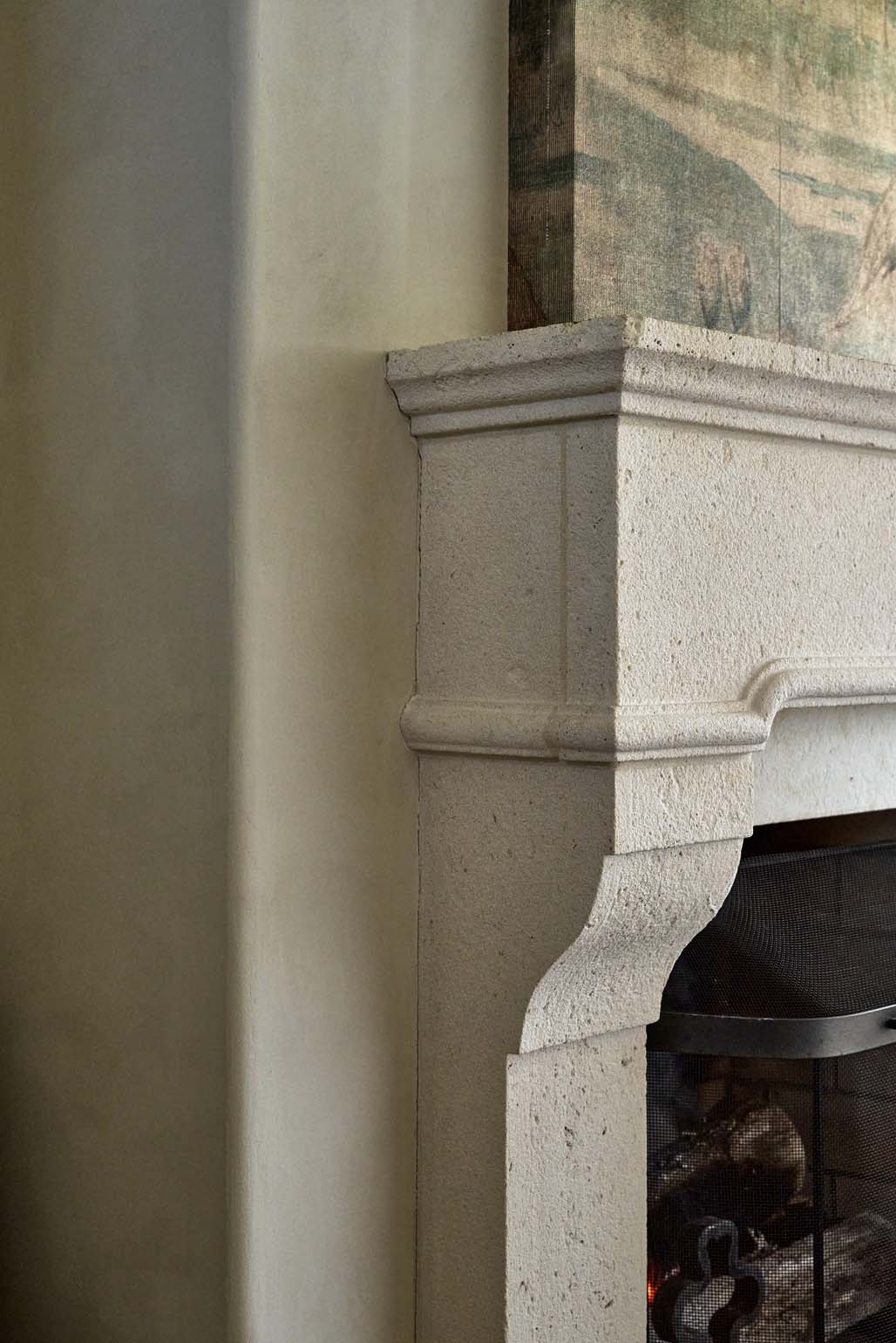 Detail of carved limestone fireplace mantel corner and iron screen
