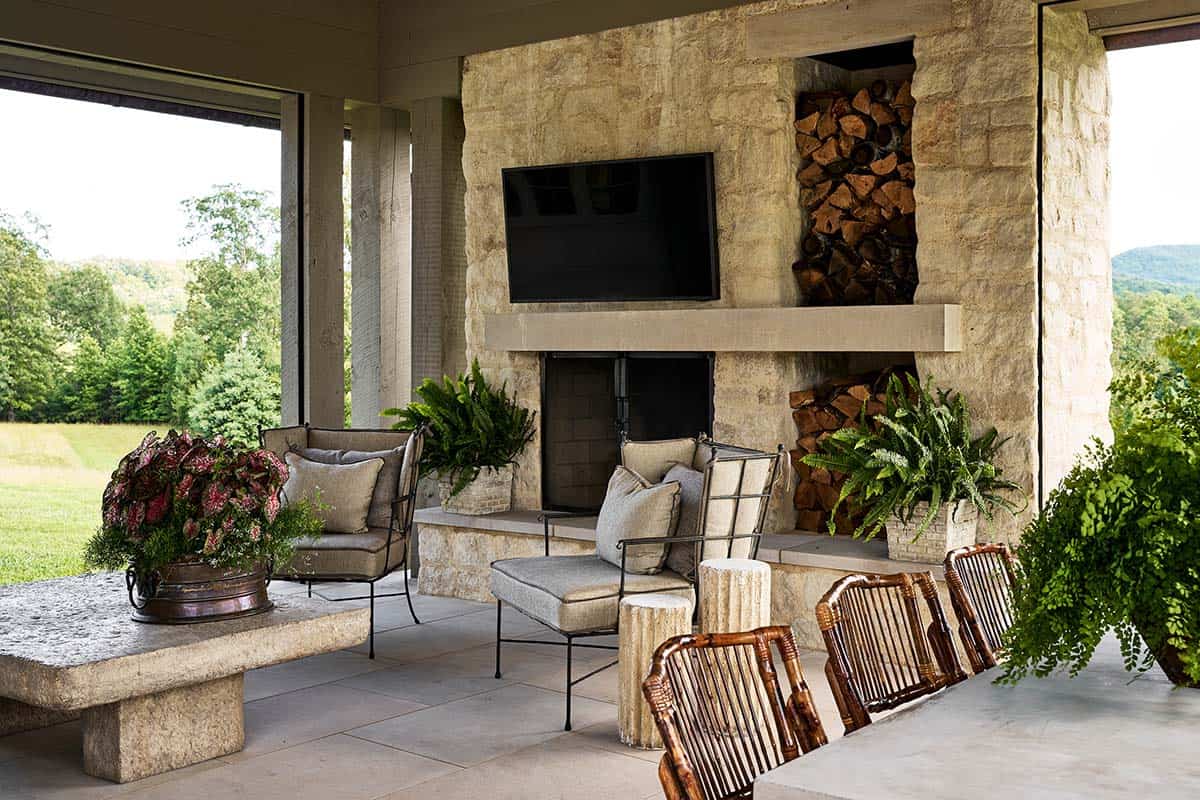Outdoor stone fireplace with mounted TV, firewood niche and rattan chairs